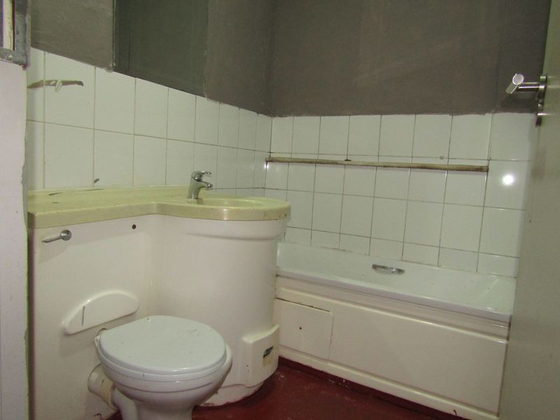 A compact bathroom featuring an integrated vanity unit, bathtub, and toilet, currently requiring significant cosmetic updates and finishing to the wall surfaces.