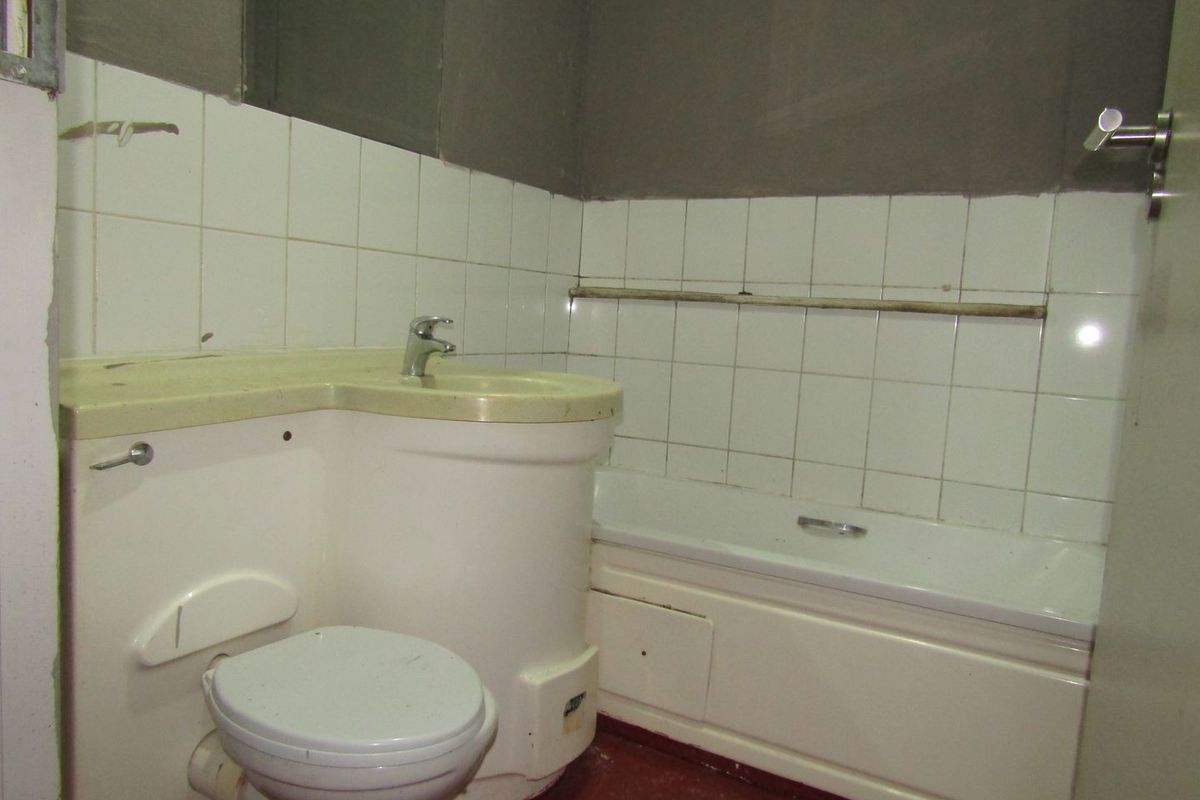 A compact bathroom featuring an integrated vanity unit, bathtub, and toilet, currently requiring significant cosmetic updates and finishing to the wall surfaces.