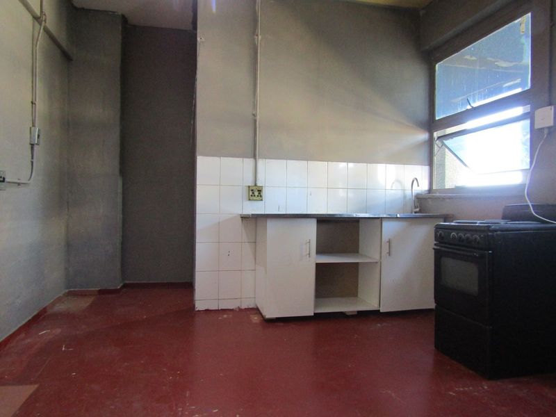 A basic, empty kitchen area featuring a sink, base cabinetry, tiled splashback, and a stove, requiring significant renovation and cosmetic updates.