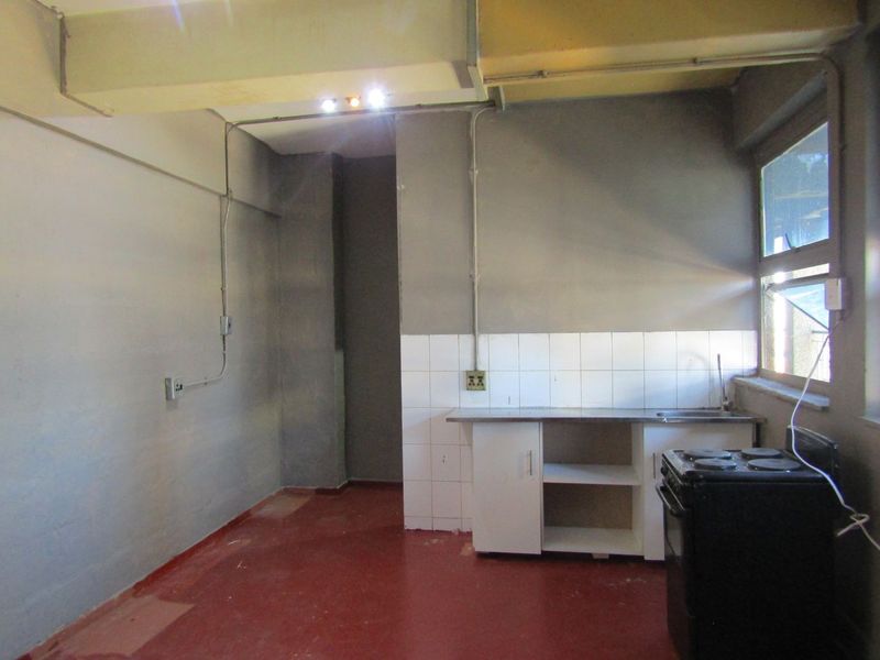 A basic, empty kitchen area featuring a stainless steel sink, tiled splashback, and exposed electrical conduit, requiring significant renovation and cosmetic updates.