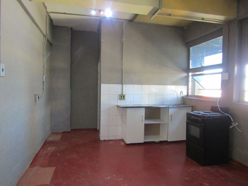 A basic, functional kitchen area featuring a sink, tiled splashback, base cabinetry, and a freestanding stove, requiring cosmetic updates and finish improvements.