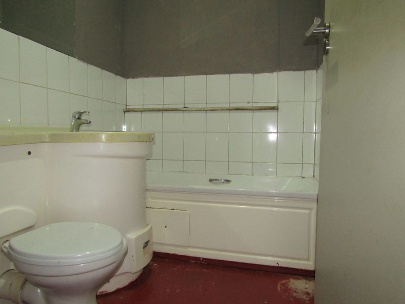 A dated bathroom featuring a built-in bathtub, toilet, and vanity basin with tiled splashbacks, requiring cosmetic updates and floor refinishing.