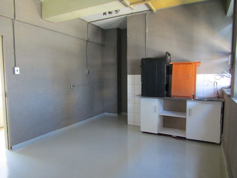 A basic, unfinished kitchen area featuring a small sink unit, base cabinetry, and exposed electrical conduit, offering significant potential for renovation.