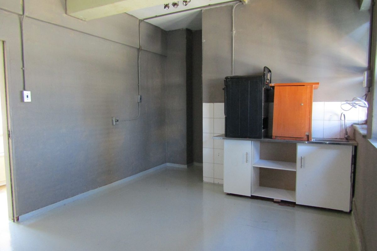 A basic, unfinished kitchen area featuring a small sink unit, base cabinetry, and exposed electrical conduit, offering significant potential for renovation.