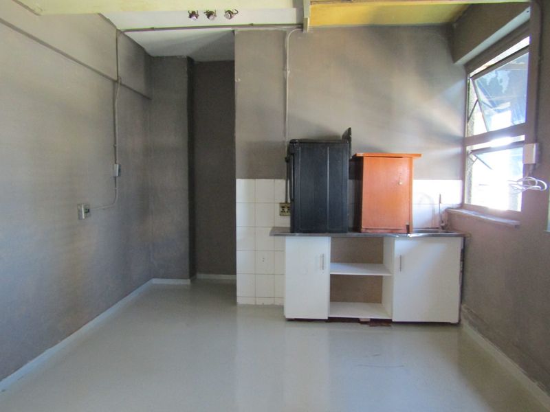 A basic, unfinished kitchen area featuring a small sink unit, tiled splashback, and exposed electrical infrastructure, requiring significant renovation and cosmetic updates.