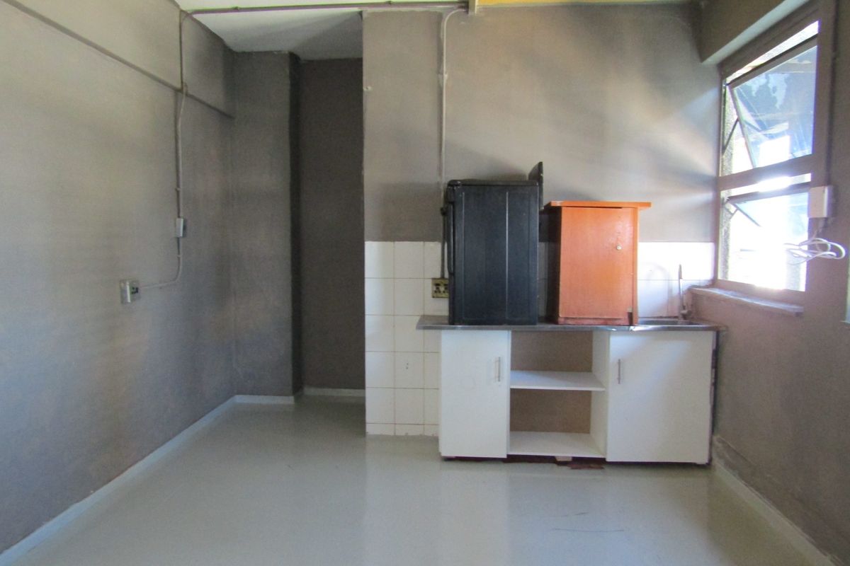 A basic, unfinished kitchen area featuring a small sink unit, tiled splashback, and exposed electrical infrastructure, requiring significant renovation and cosmetic updates.