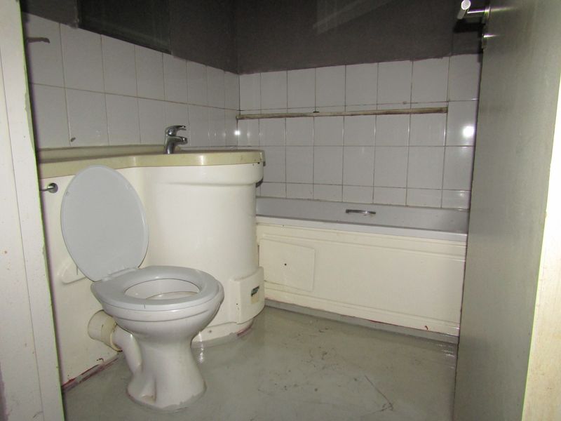 A dated bathroom featuring an integrated vanity basin, toilet, and bathtub with wall tiling, requiring significant refurbishment and cosmetic updates.