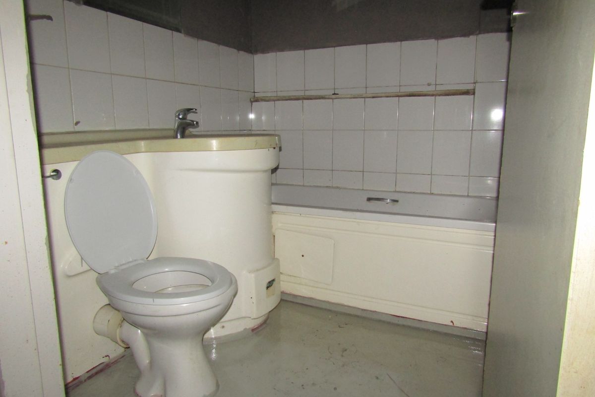 A dated bathroom featuring an integrated vanity basin, toilet, and bathtub with wall tiling, requiring significant refurbishment and cosmetic updates.