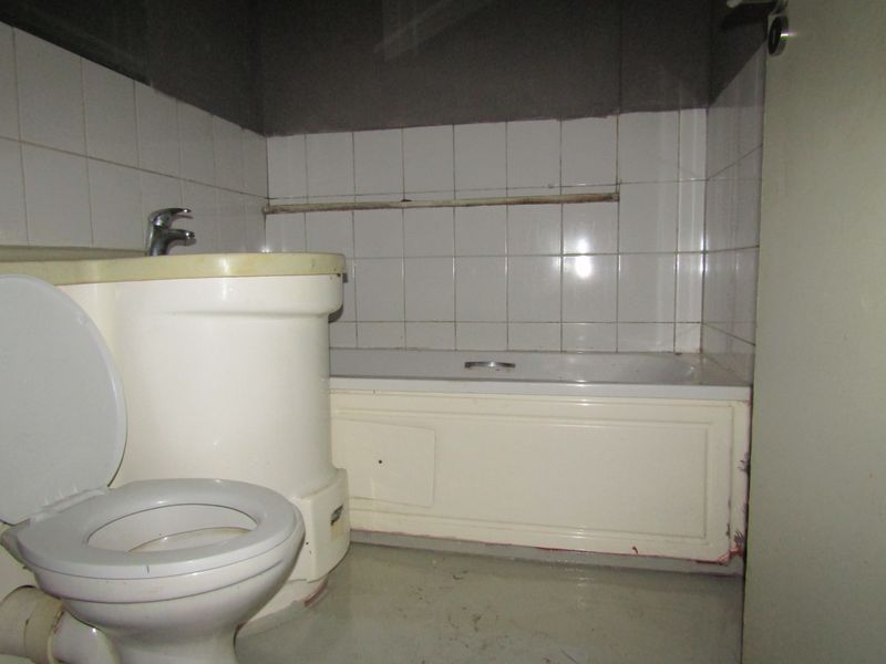 A dated bathroom featuring a standard bathtub, toilet, and basin with tiled walls, requiring significant renovation and cosmetic updates.