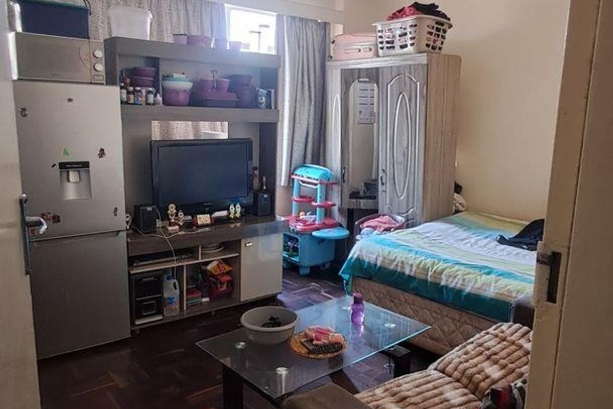 A bedroom featuring parquet flooring and large windows with curtain tracks, offering a functional living space.