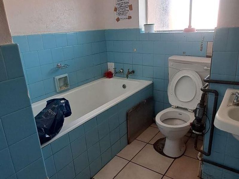 A dated bathroom featuring a bathtub, pedestal sink, and toilet with blue wall tiling and ceramic floor tiles, requiring modernization.