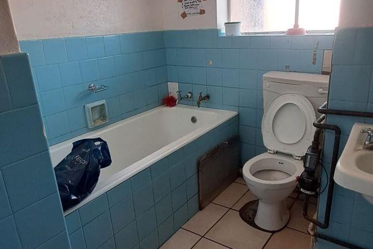 A dated bathroom featuring a bathtub, pedestal sink, and toilet with blue wall tiling and ceramic floor tiles, requiring modernization.