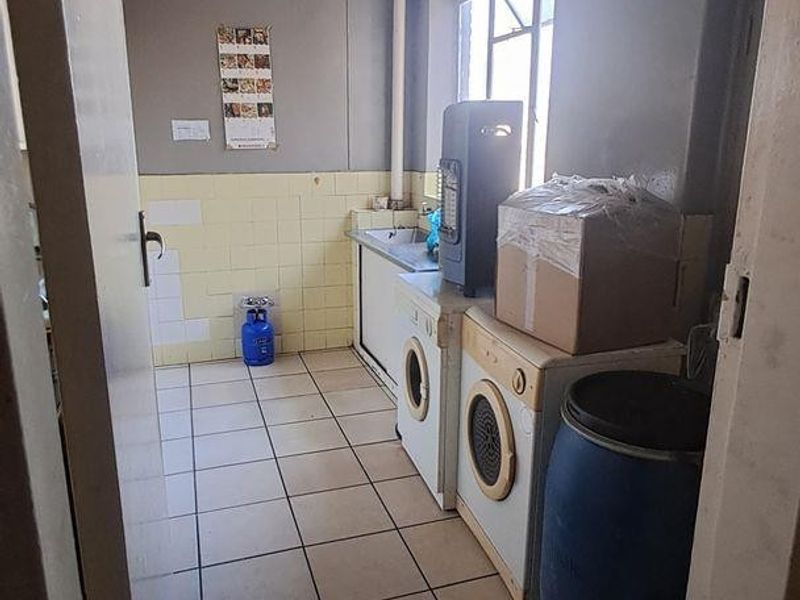 A functional laundry area featuring tiled flooring, wall tiling, and a built-in sink, requiring cosmetic updates to improve its overall condition.