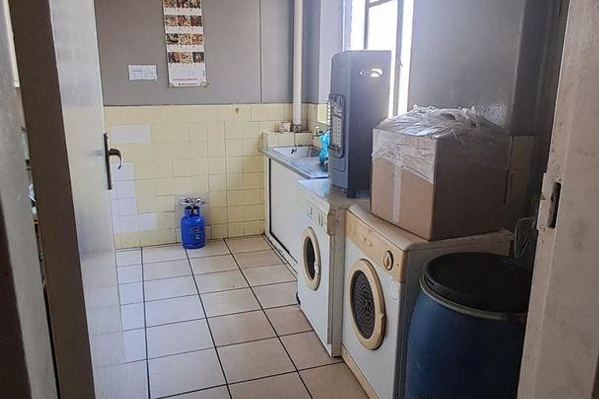 A functional laundry area featuring tiled flooring, wall tiling, and a built-in sink, requiring cosmetic updates to improve its overall condition.