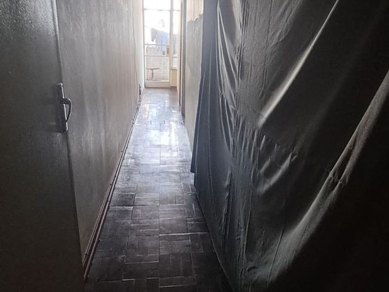 A narrow hallway featuring original parquet flooring, leading towards a glass door with access to an outdoor balcony area.