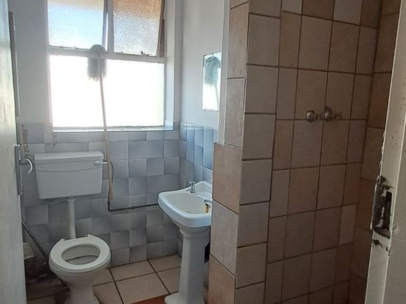 A dated bathroom featuring a pedestal basin, toilet, and shower with tiled finishes, requiring renovation to update the fixtures and address surface wear.