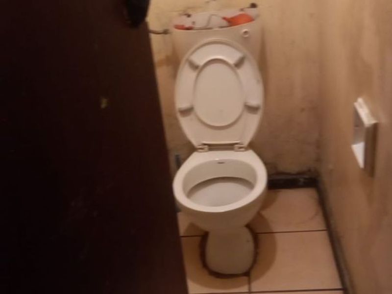 A small, dated bathroom featuring a toilet and tiled flooring, currently requiring significant cosmetic repairs and wall refinishing.