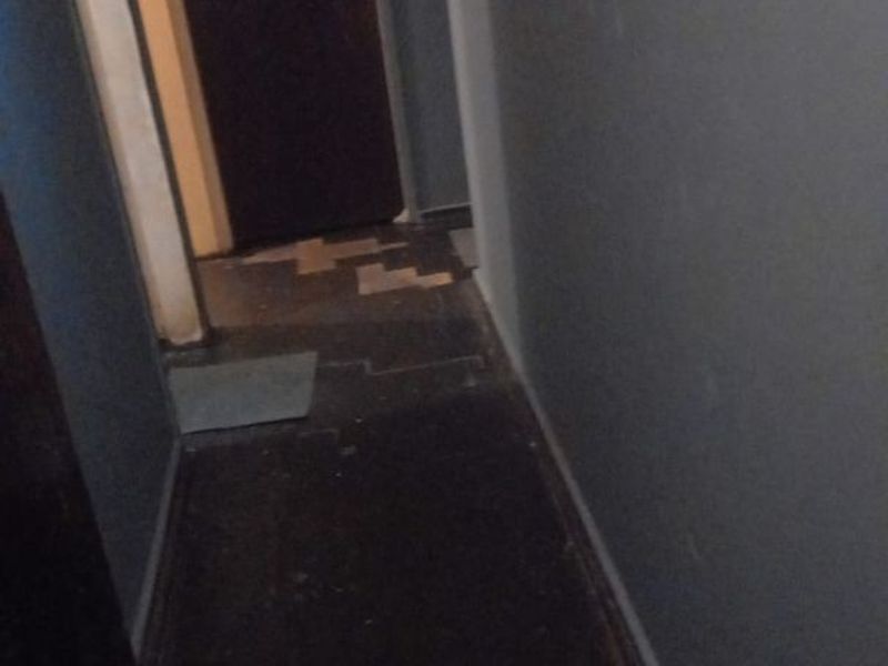 A narrow interior hallway showing signs of wear, including damaged flooring and missing tiles, requiring maintenance or renovation.