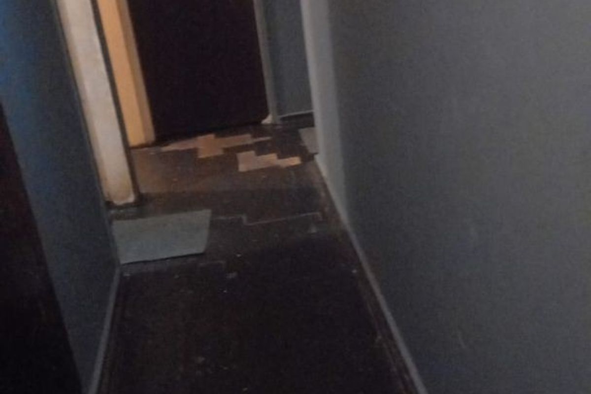 A narrow interior hallway showing signs of wear, including damaged flooring and missing tiles, requiring maintenance or renovation.