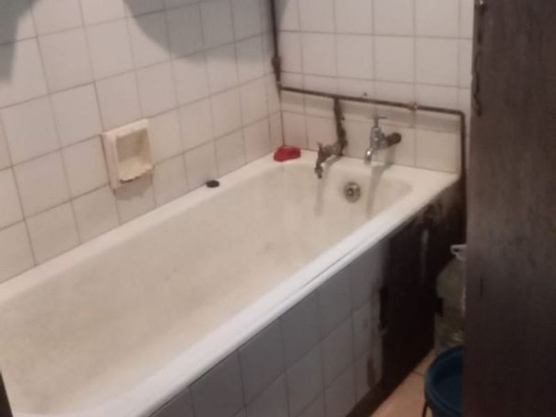 A dated bathroom featuring a bathtub with exposed plumbing and tiled finishes, currently requiring maintenance and cosmetic updates.