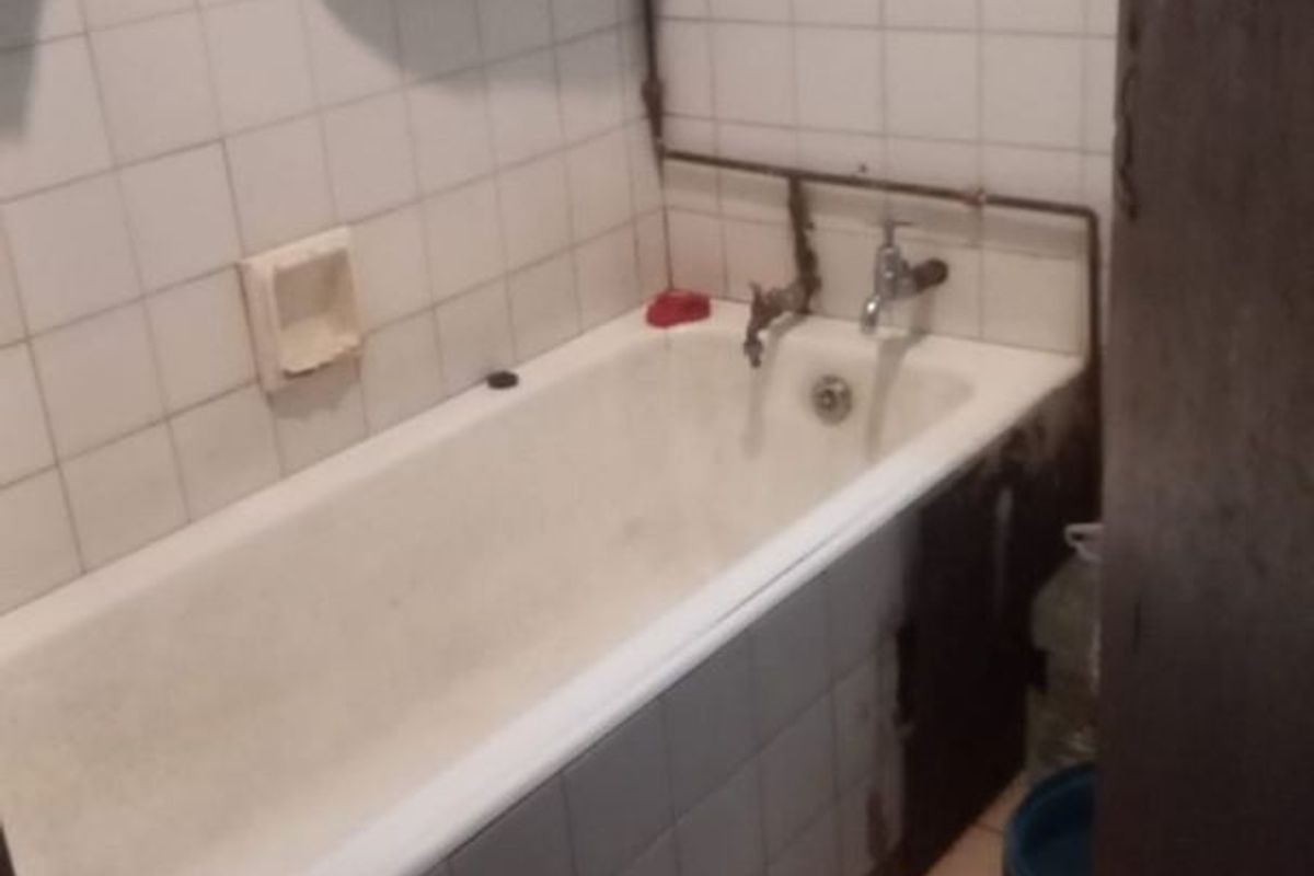 A dated bathroom featuring a bathtub with exposed plumbing and tiled finishes, currently requiring maintenance and cosmetic updates.