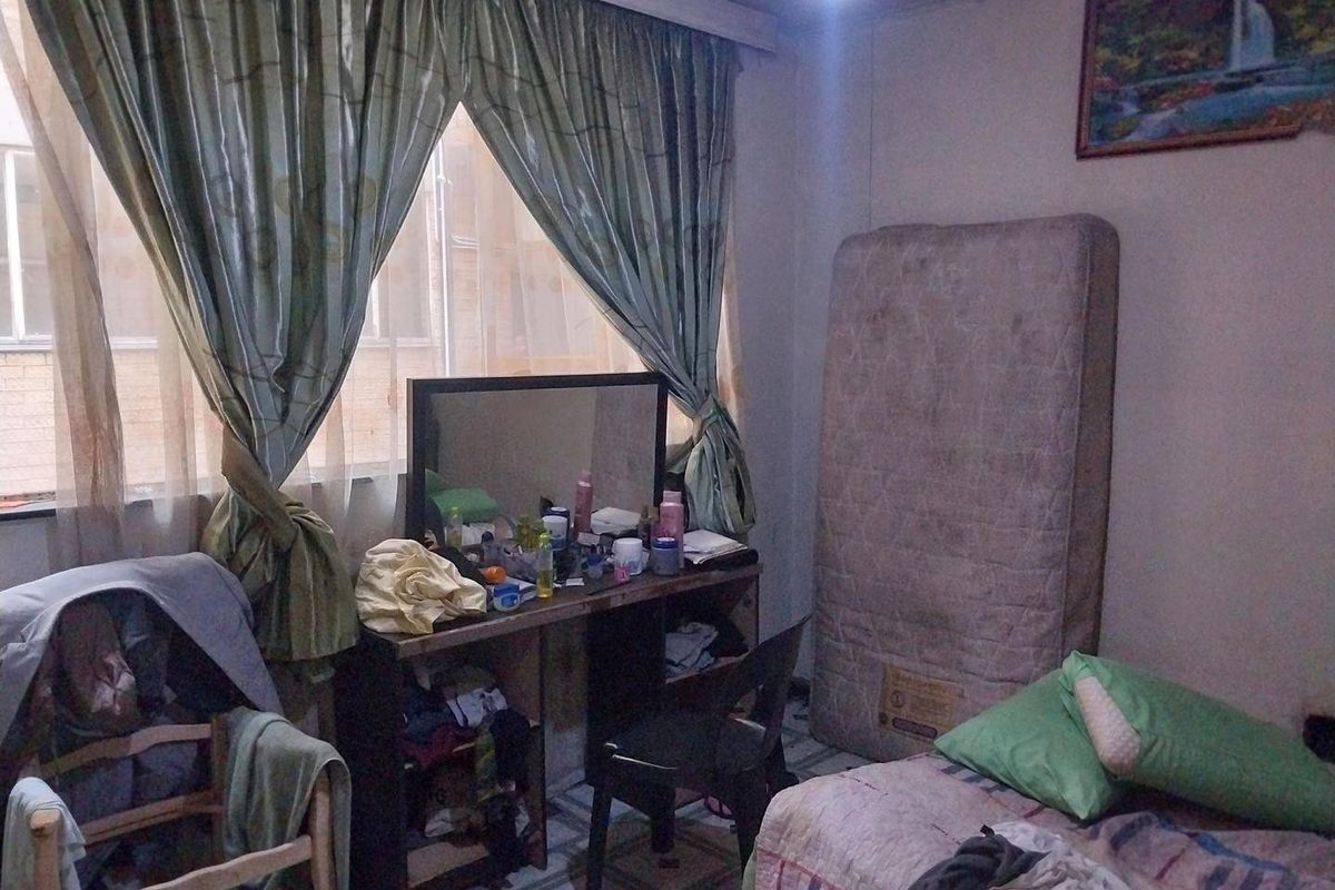 A bedroom featuring tiled flooring and large windows with curtain treatments, requiring cosmetic updates to improve its overall appeal and condition.