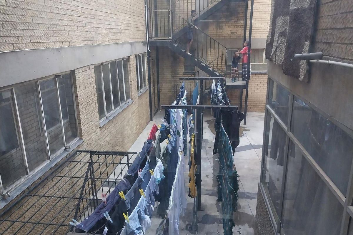 A rear courtyard area of an apartment building featuring a metal fire escape staircase and communal laundry drying facilities.