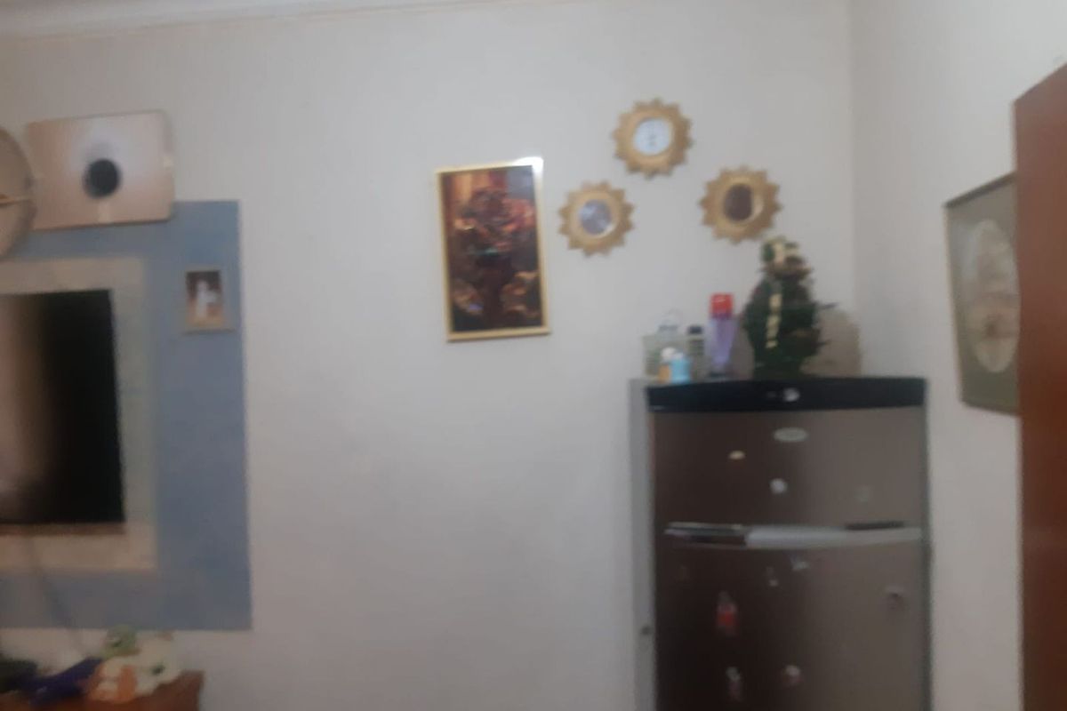 A blurry interior view of a living area featuring wall-mounted decor and a refrigerator.