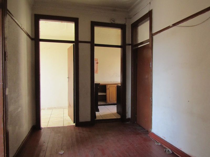 A vacant hallway featuring original timber flooring and door frames, showing signs of wear and requiring cosmetic refurbishment.