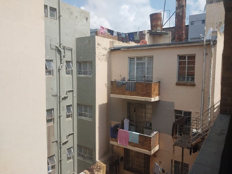 Rear view of an apartment building complex showing multiple balconies, external plumbing, and weathered brick facades with visible signs of wear.