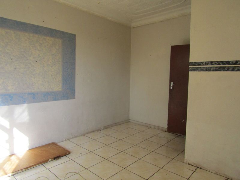An empty living room featuring ceramic floor tiles, neutral wall finishes, and a standard internal door, ready for renovation or staging.