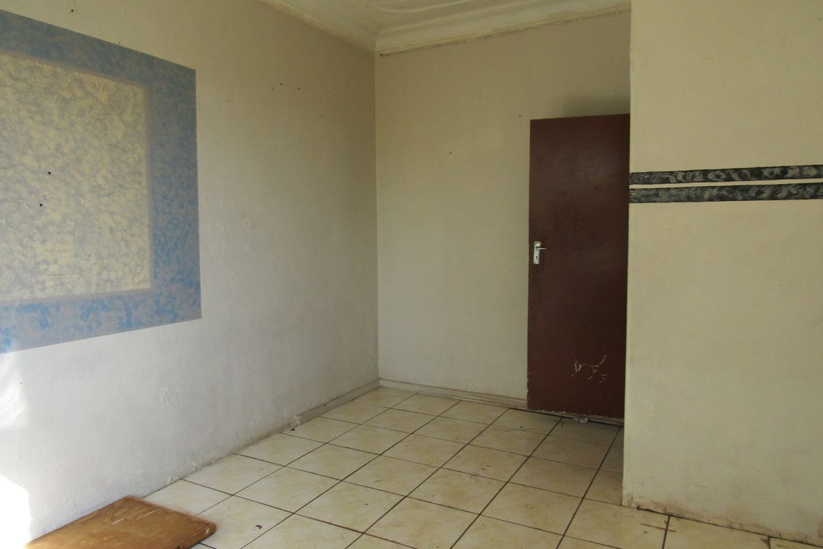 An empty bedroom featuring tiled flooring and a simple interior door, requiring cosmetic updates to improve its overall appeal.