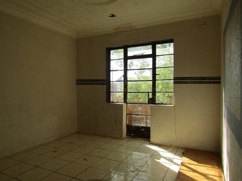 An empty bedroom featuring tiled flooring, decorative ceiling cornices, and a steel-framed window with visible glass damage.