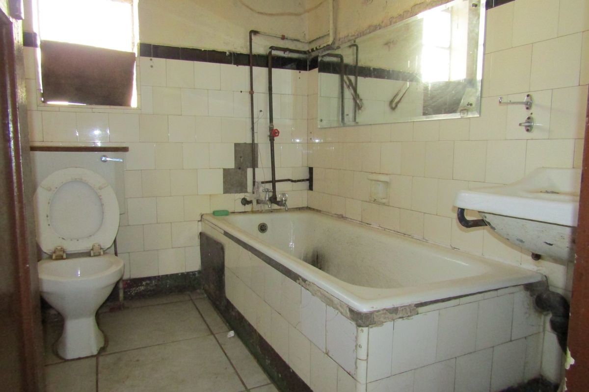A dated bathroom requiring significant renovation, featuring a bathtub, toilet, and wall-mounted basin with visible wear and missing tile finishes.