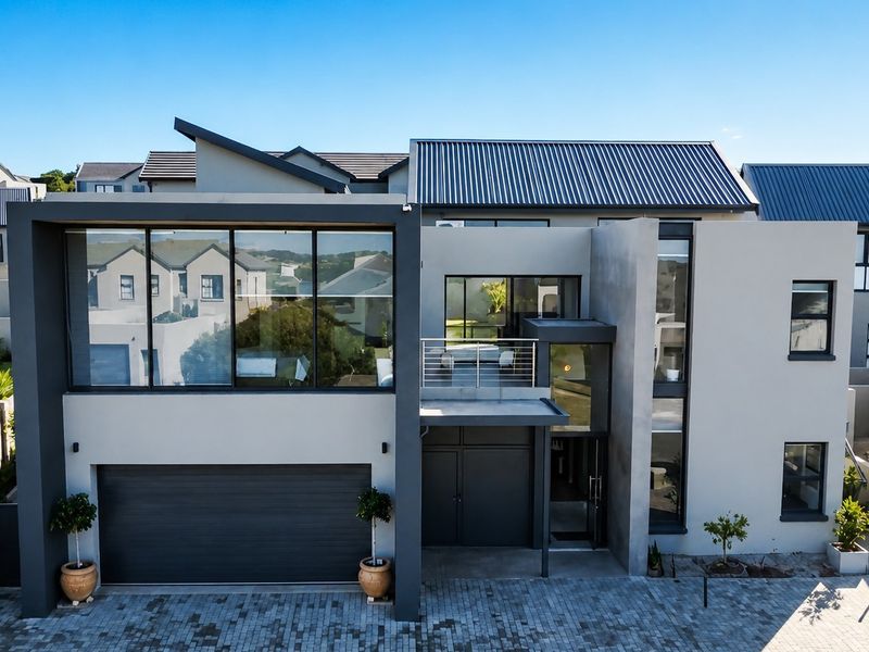 Modern double-story residential property featuring a double garage, paved driveway, large glass windows, and a balcony with steel balustrades.