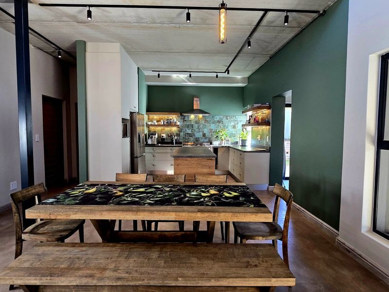 Modern open-plan living and kitchen area featuring an exposed concrete ceiling, track lighting, and a stylish kitchen with a central island and tiled backsplash.