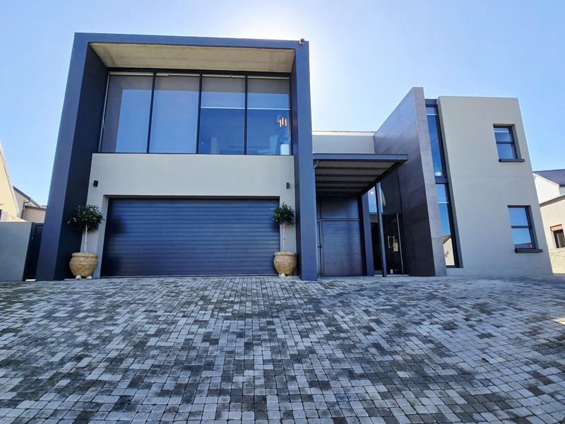 Modern double-story residential facade featuring a paved driveway, integrated double garage, and contemporary architectural design with large glass windows.