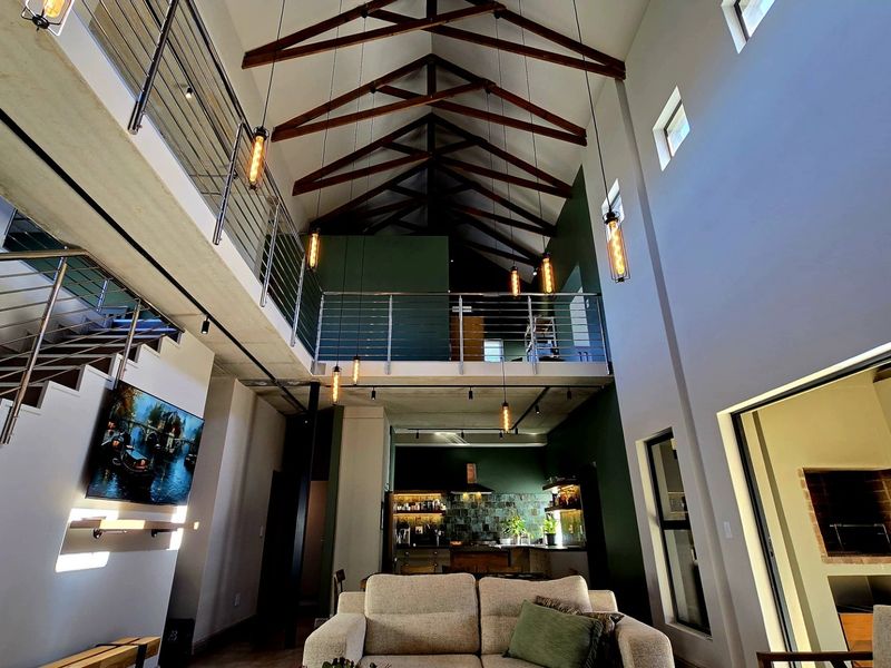 Spacious open-plan living area featuring a double-volume ceiling with exposed timber trusses, a mezzanine level, and modern industrial-style finishes.