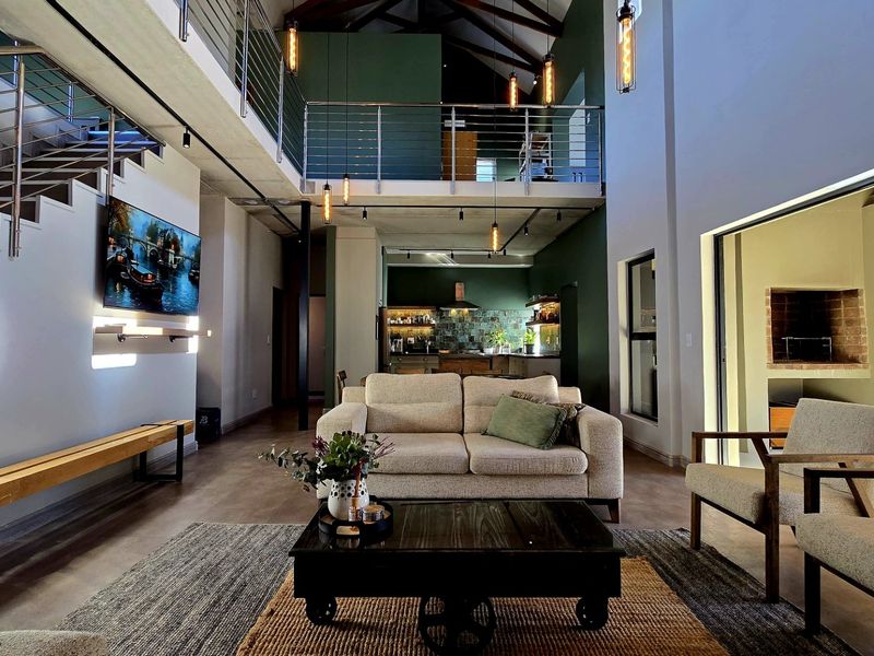 Spacious open-plan living area featuring a double-volume ceiling with exposed trusses, a mezzanine level, modern kitchen, and an integrated indoor fireplace.