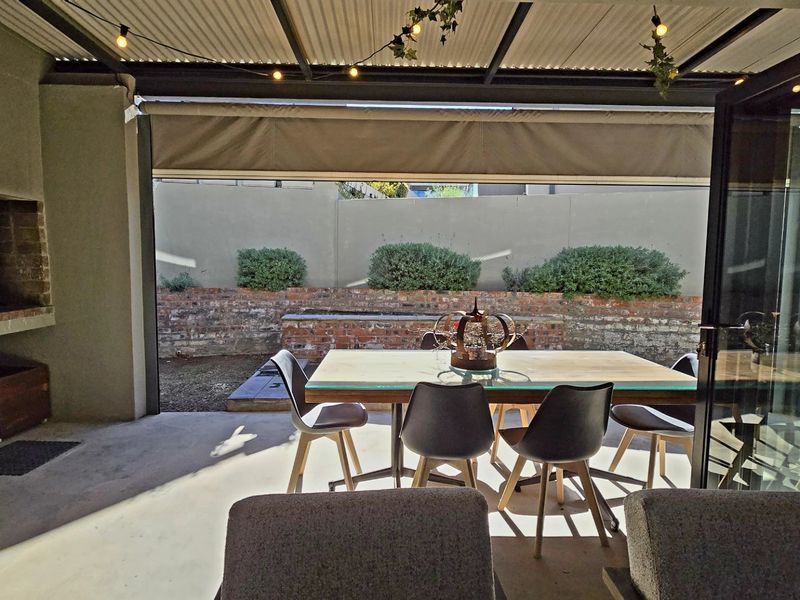 Covered outdoor patio featuring a built-in braai, concrete flooring, and bi-fold doors leading to a landscaped garden with a brick retaining wall.