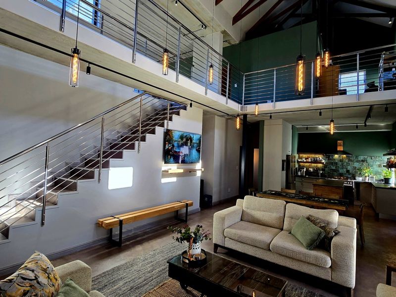 Spacious open-plan living area featuring a mezzanine level, modern stainless steel staircase, exposed timber beams, and a contemporary kitchen with high-end finishes.