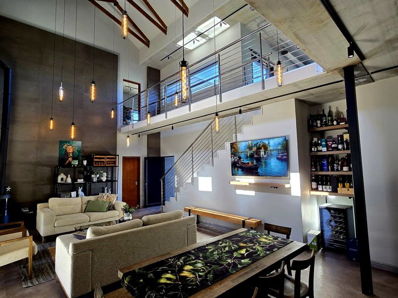 Spacious open-plan living area featuring double-volume ceilings with exposed timber rafters, a mezzanine level, modern staircase, and integrated wine storage.
