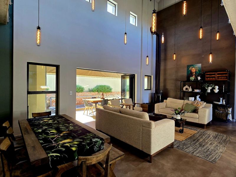 Spacious open-plan living and dining area featuring double volume ceilings, an exposed concrete feature wall, wood-burning fireplace, and seamless access to the patio.