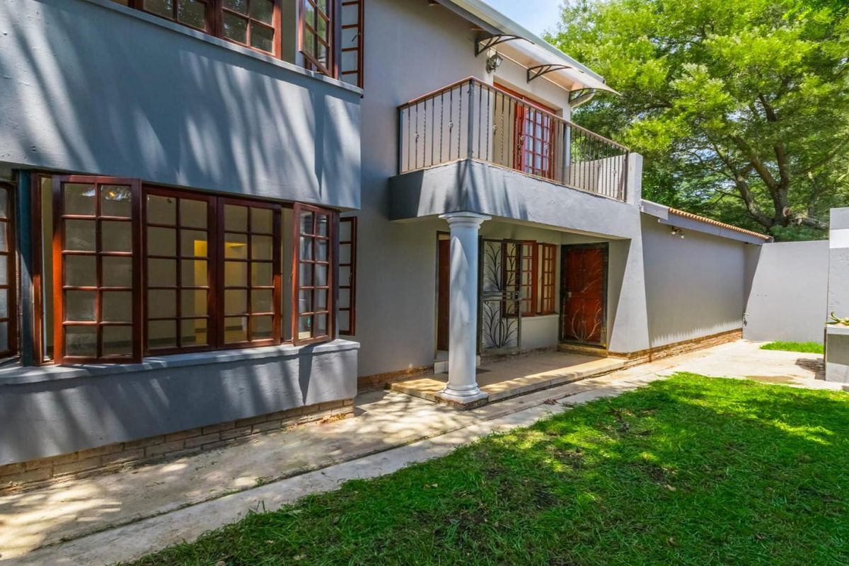 Rear view of a two-story house featuring a balcony with metal railing, a covered patio area, and a small garden with a paved walkway.