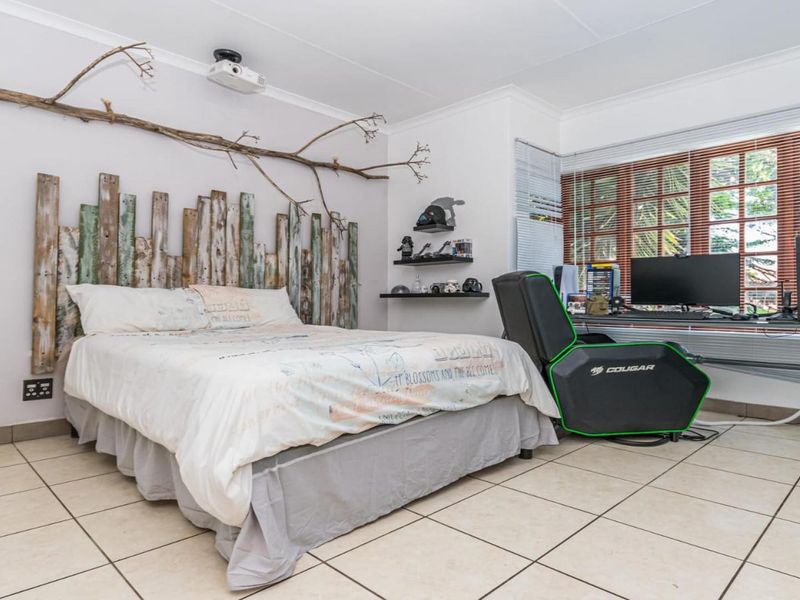 A bedroom featuring tiled flooring, ceiling-mounted projector, and built-in shelving, offering a functional space with natural light through venetian blinds.