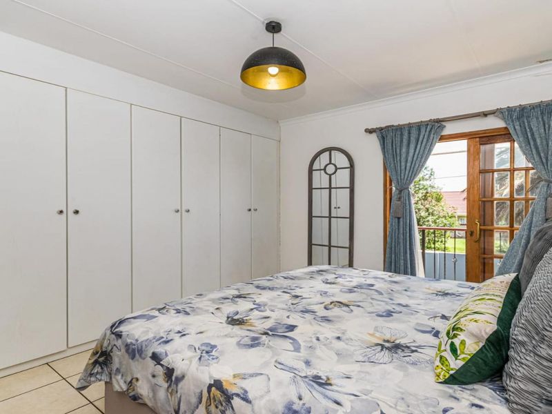 A well-maintained bedroom featuring extensive built-in cupboards, tiled flooring, and a timber-framed glass door providing access to an outdoor area.