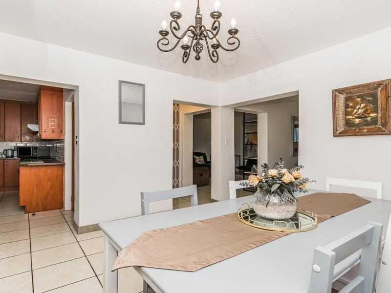 A dining area featuring tiled flooring and a classic chandelier, with an open-plan flow leading into the adjacent kitchen.