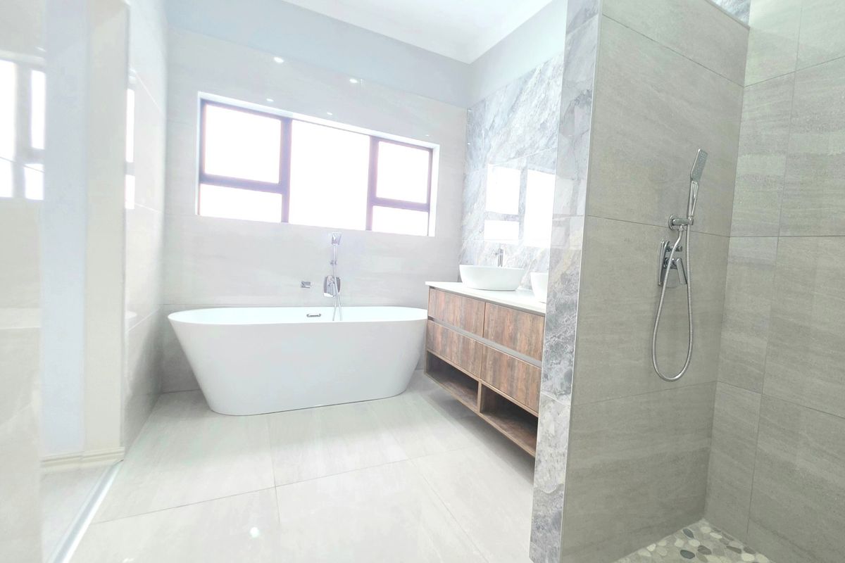 Modern bathroom featuring a freestanding bathtub, double vanity with vessel sinks, and a spacious walk-in shower with pebble flooring and contemporary tiling.