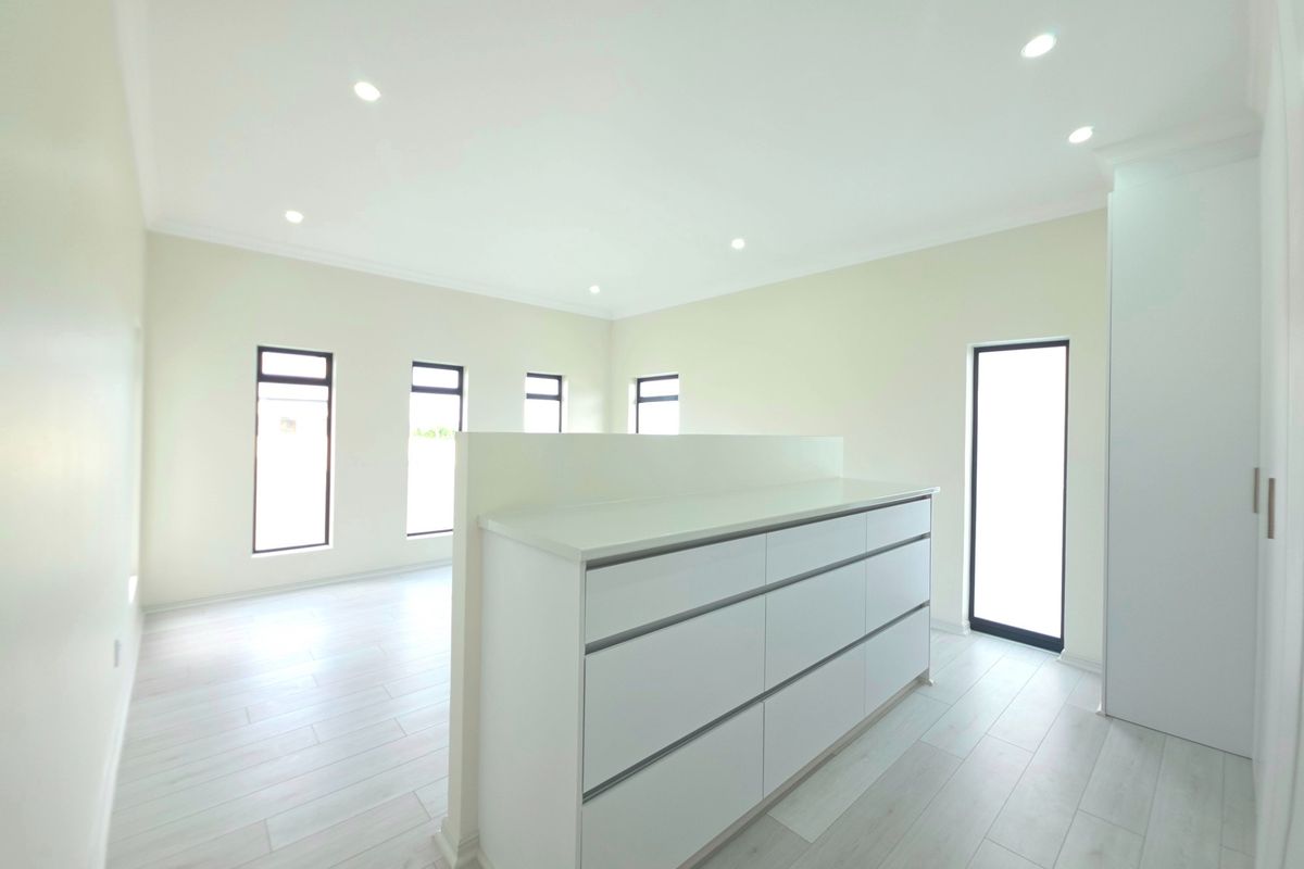 A bright, modern, and empty bedroom featuring built-in cabinetry, light-toned laminate flooring, and multiple windows providing ample natural light.