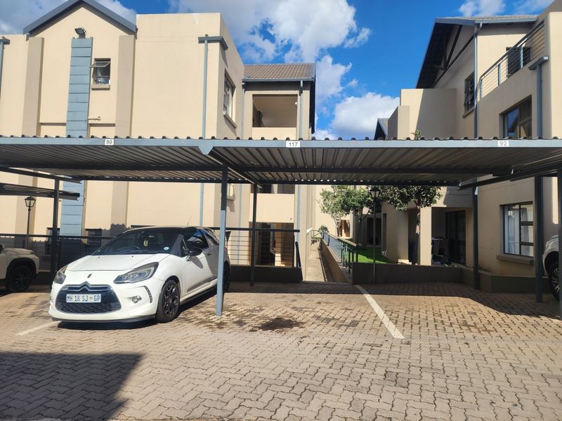 A covered carport area with paved driveway and steel structure located within an apartment complex.